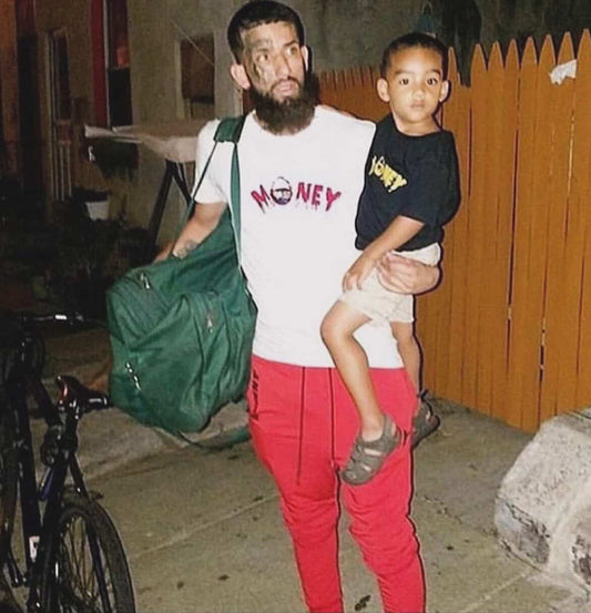 Man holding a child outdoors with a green bag 